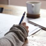 Quality Coffee - person writing on brown wooden table near white ceramic mug