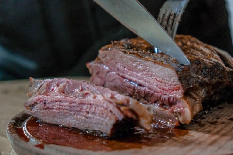 Over-Roasted - person slicing juicy medium rare meat on top of brown wooden cutting board